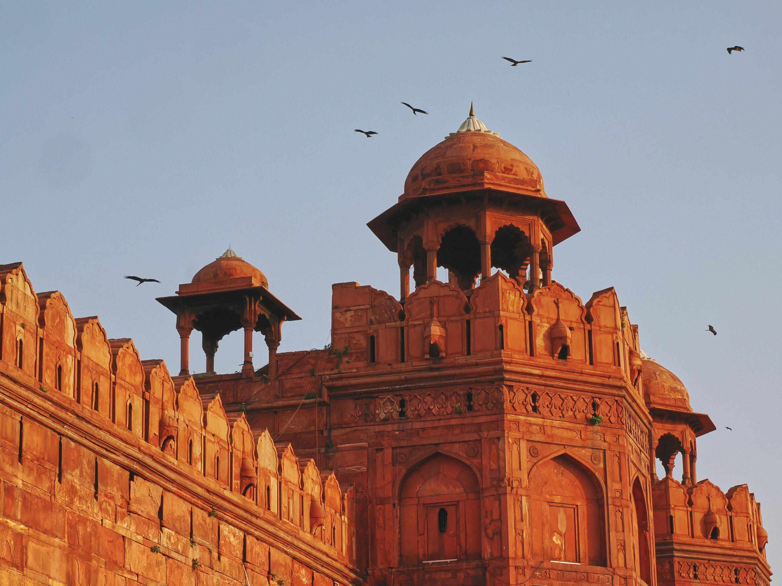 Close-up of Red Fort's intricate architecture at sunset with flying birds.